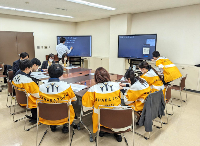 写真:矢巾町職員による、フューチャー・デザインを応用した、都市計画マスタープランのアセスメント実践の様子(現世代グループと、法被を着た仮想将来世代グループの合意形成セッション) 写真:矢巾町職員による、フューチャー・デザインを応用した、都市計画マスタープランのアセスメント実践の様子(現世代グループと、法被を着た仮想将来世代グループの合意形成セッション)